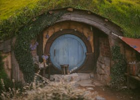 Rustic hobbit-style cottage with wooden door surrounded by lush greenery and ivy.